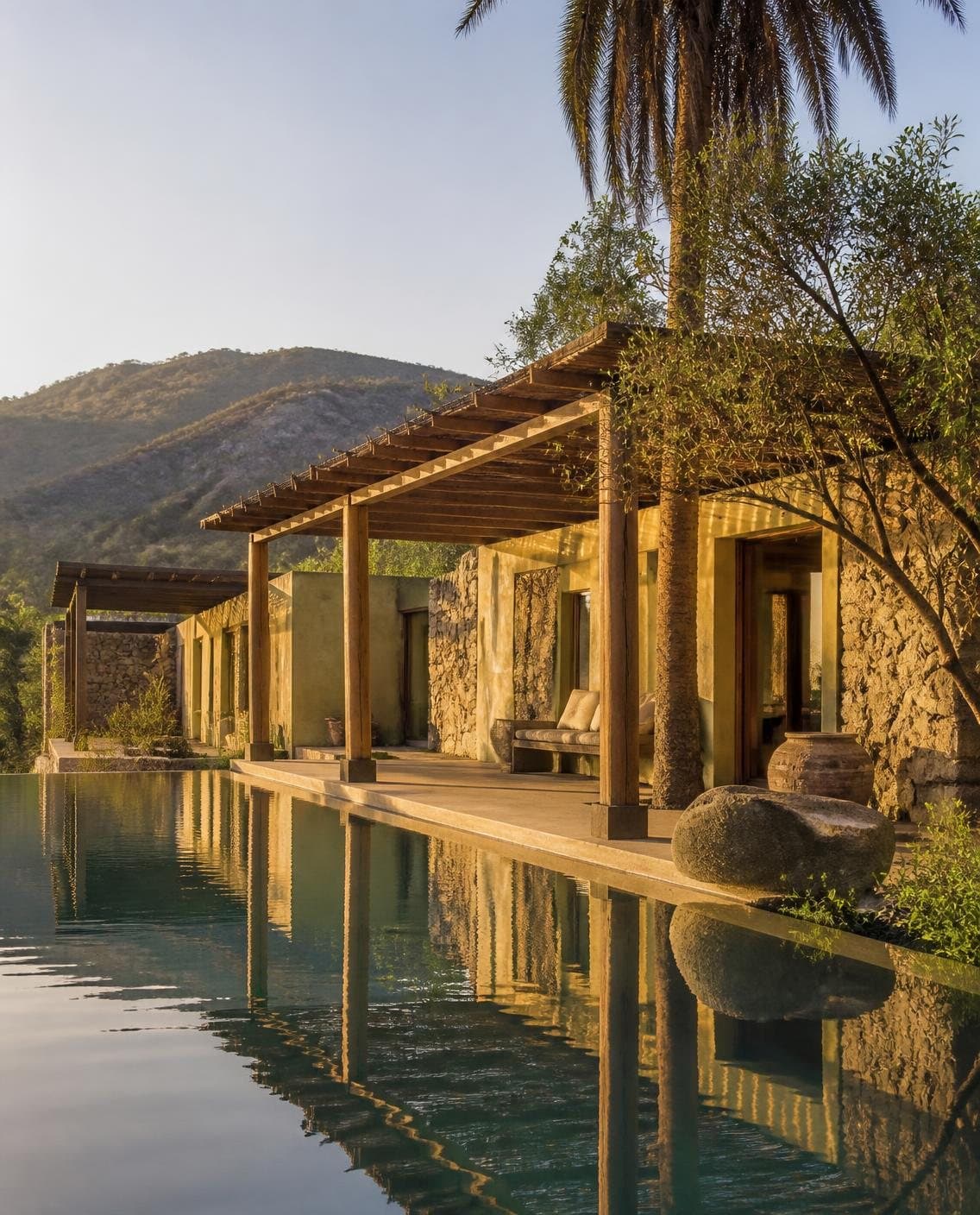 Illustrative resort pavilion of stone and plaster with a timber pergola beside an infinity pool at golden hour
